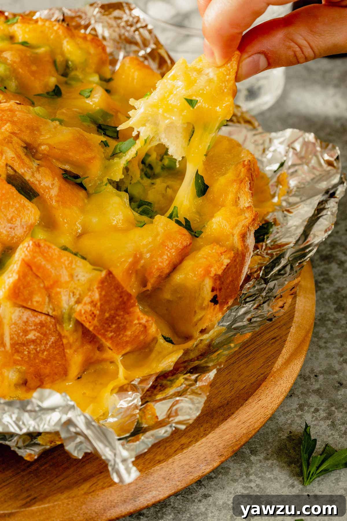 A hand pulling a piece of pull-apart bread with strings of melted cheese stretching.