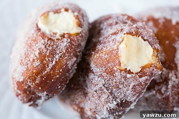 Various homemade vanilla cream-filled doughnuts on a cooling rack