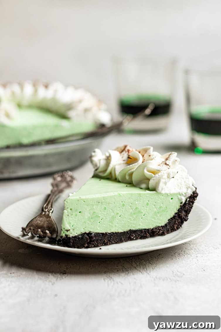 A perfectly sliced piece of grasshopper pie resting on a white plate, accompanied by a fork, highlighting its layers.