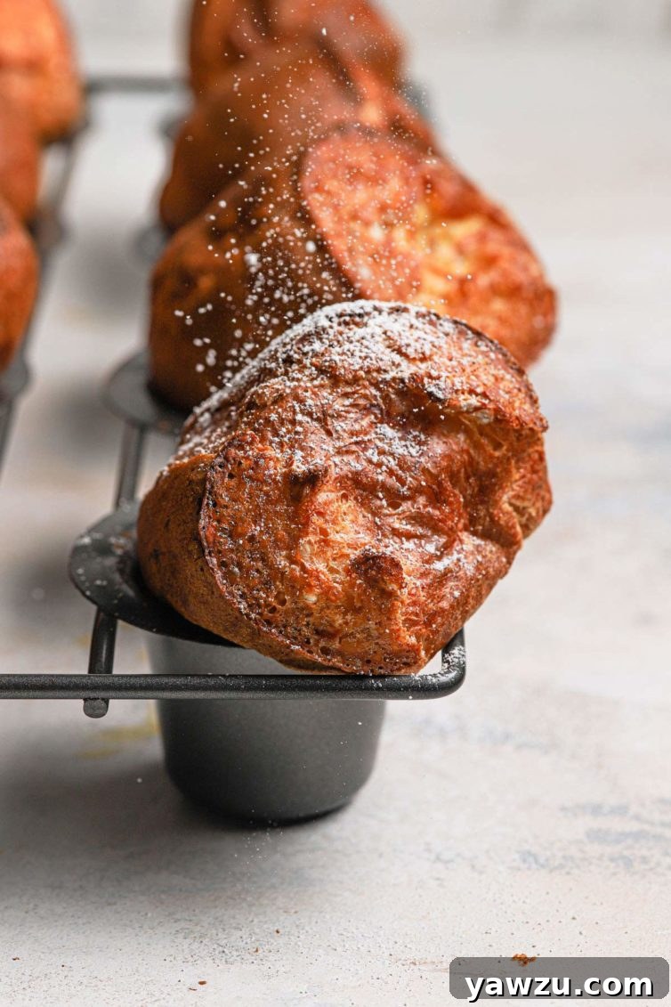 Golden brown baked breakfast popovers in a grey popover baking pan dusted with powdered sugar