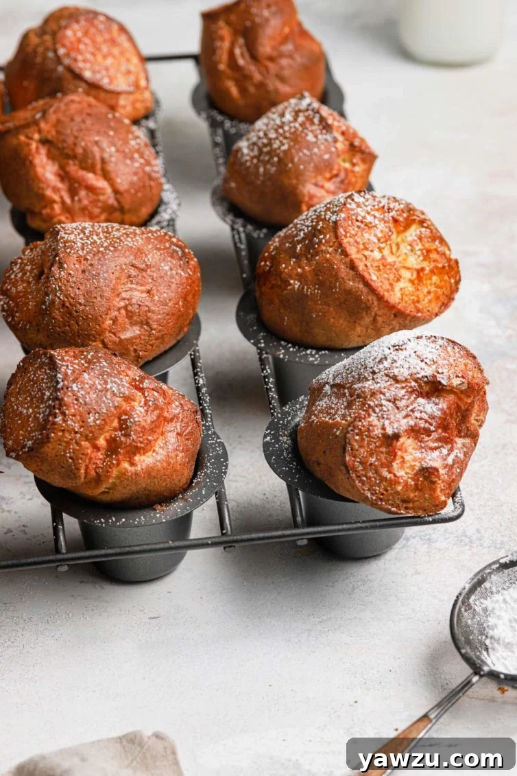 Golden brown baked breakfast popovers in a grey popover baking pan dusted with powdered sugar