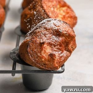 Golden brown baked breakfast popovers in a grey popover baking pan dusted with powdered sugar