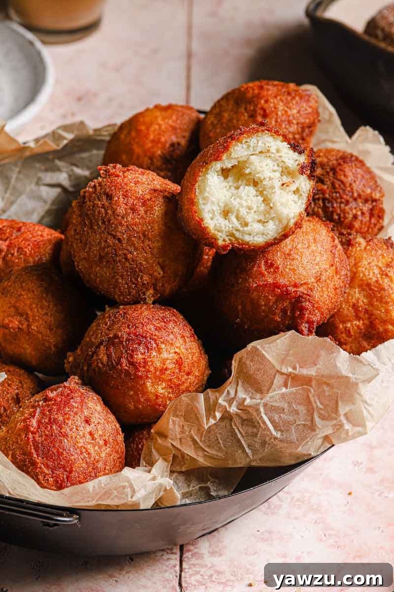 A pile of fried zeppole on parchment-lined bowl with a bite taken out of the one on top.