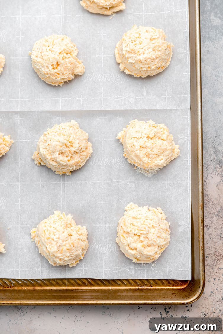 Unbaked cheddar bay biscuit dough scoops arranged on a baking sheet, spaced apart and ready for the oven.