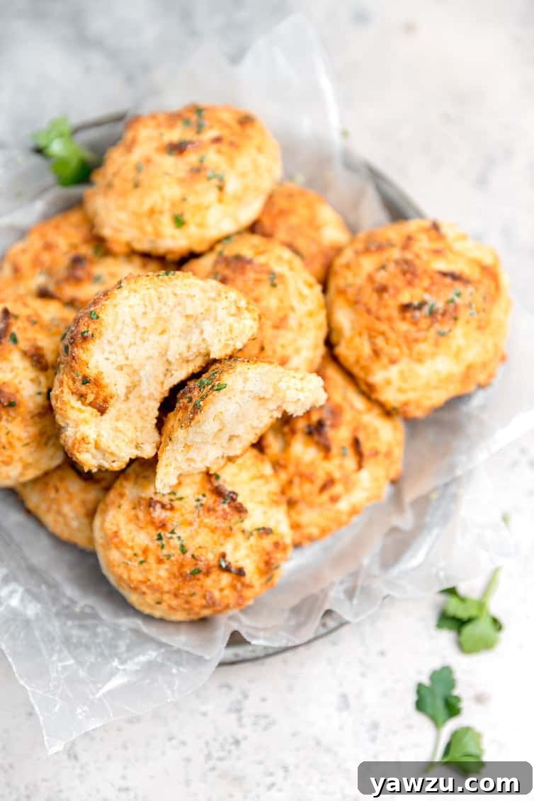 A bowl overflowing with golden-brown cheddar bay biscuits, with one biscuit broken in half to reveal its fluffy, cheesy interior.