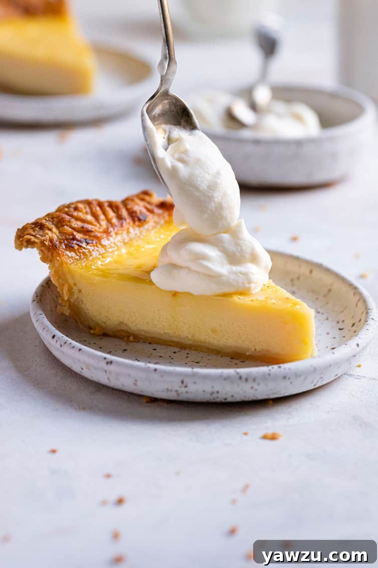 Spooning a dollop of whipped cream on slice of buttermilk pie.