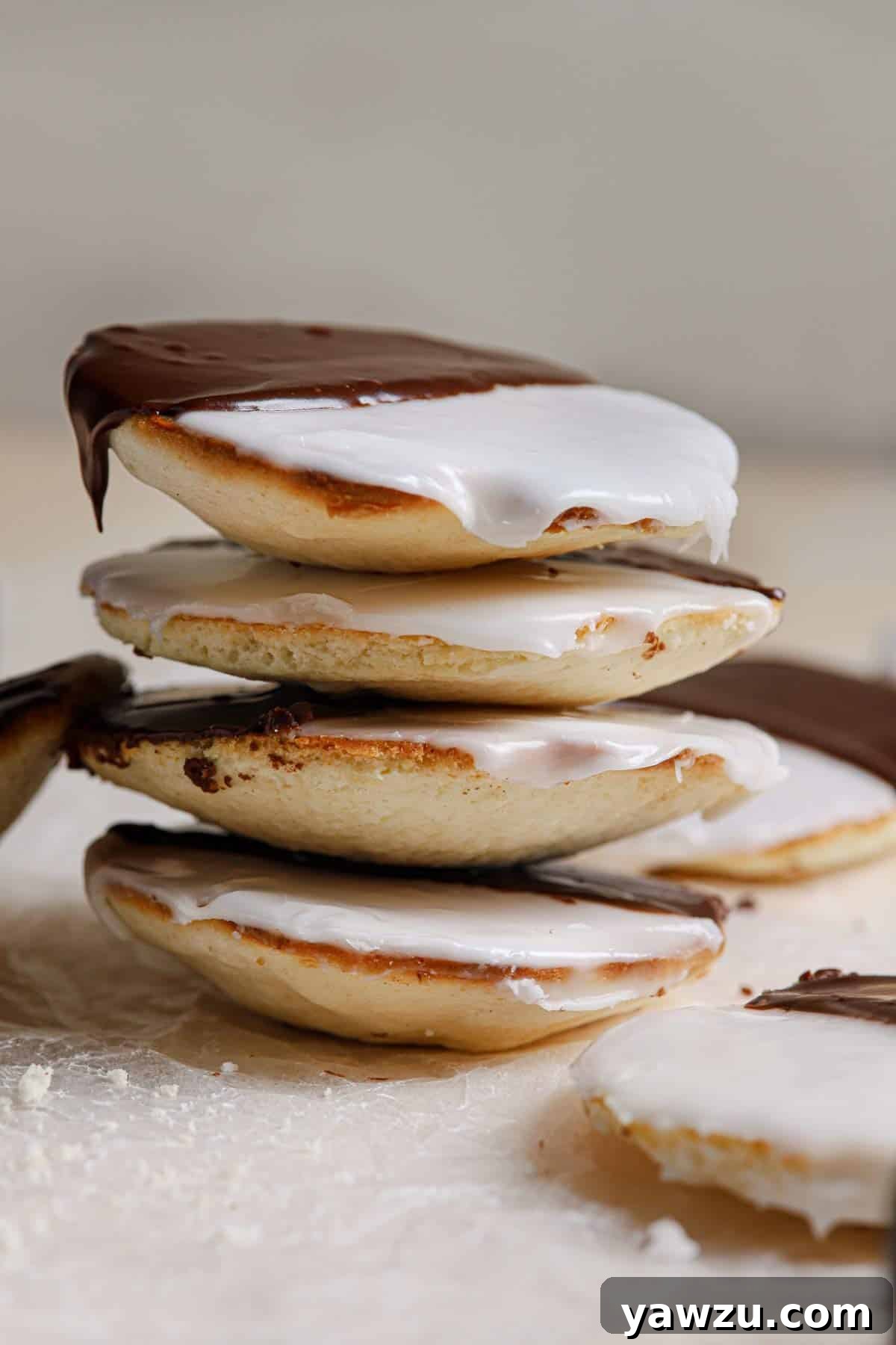 A stack of iced black and white cookies on a counter with a few on the counter below.