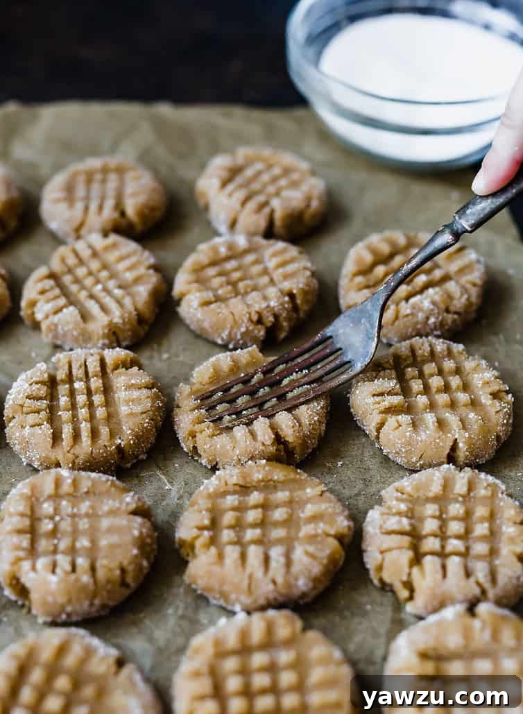 A fork pressing down on unbaked peanut butter cookie dough balls arranged on a baking sheet, creating the signature crisscross pattern.