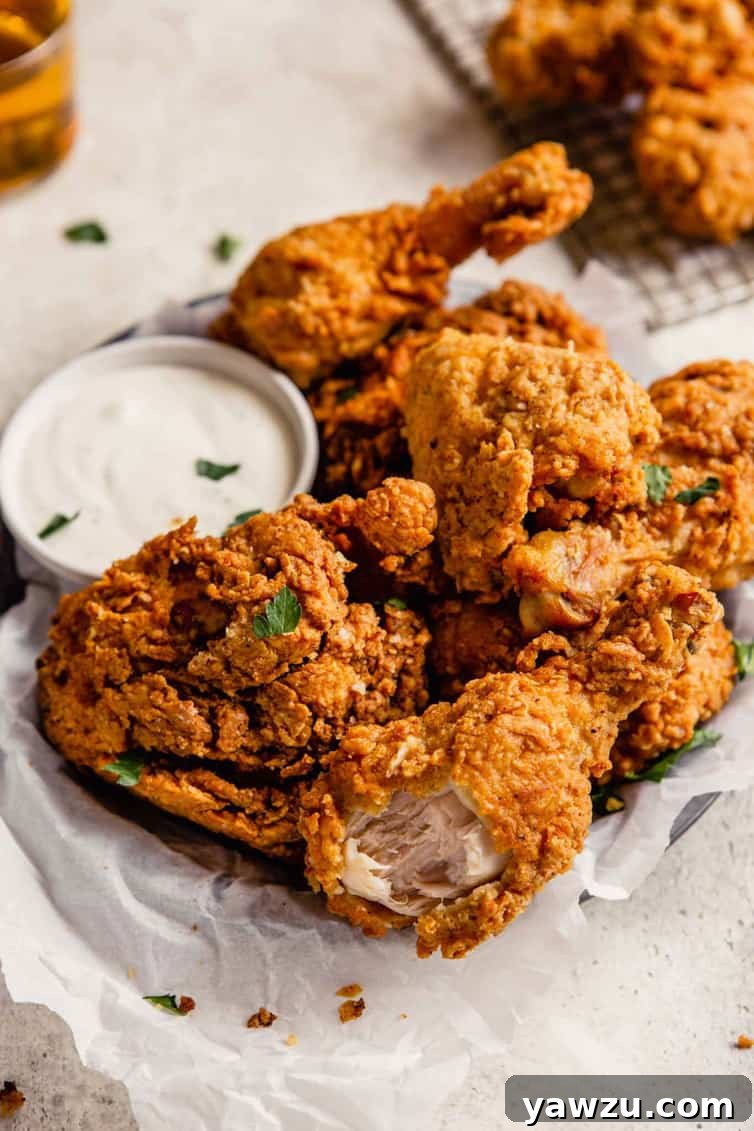 A bite taken out of a crispy piece of buttermilk fried chicken on a sliver plate lined with parchment paper.