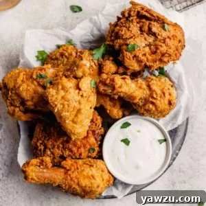 A silver plate with parchment paper topped with crispy fried chicken pieces with a small cup of ranch dressing.