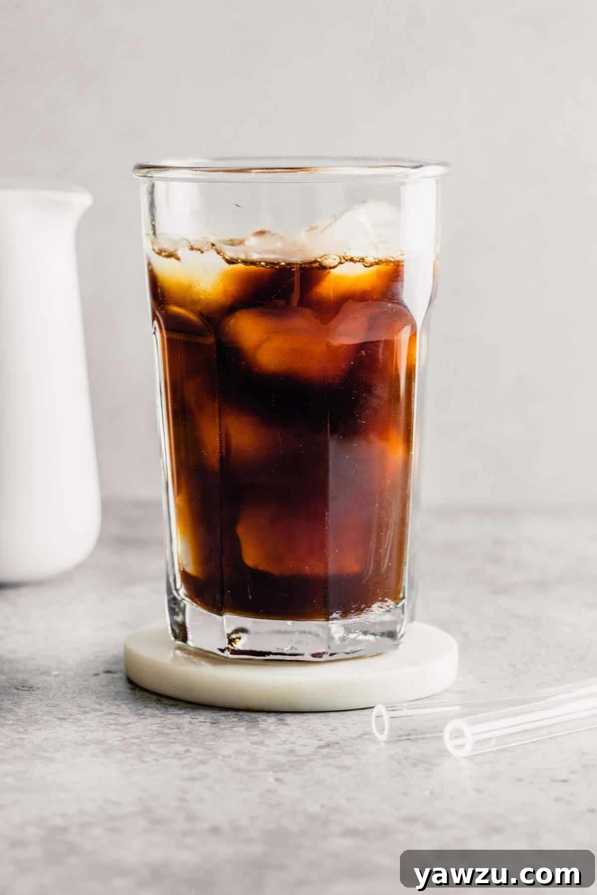 A refreshing glass of iced coffee on a wooden coaster with a pitcher of milk in the background.