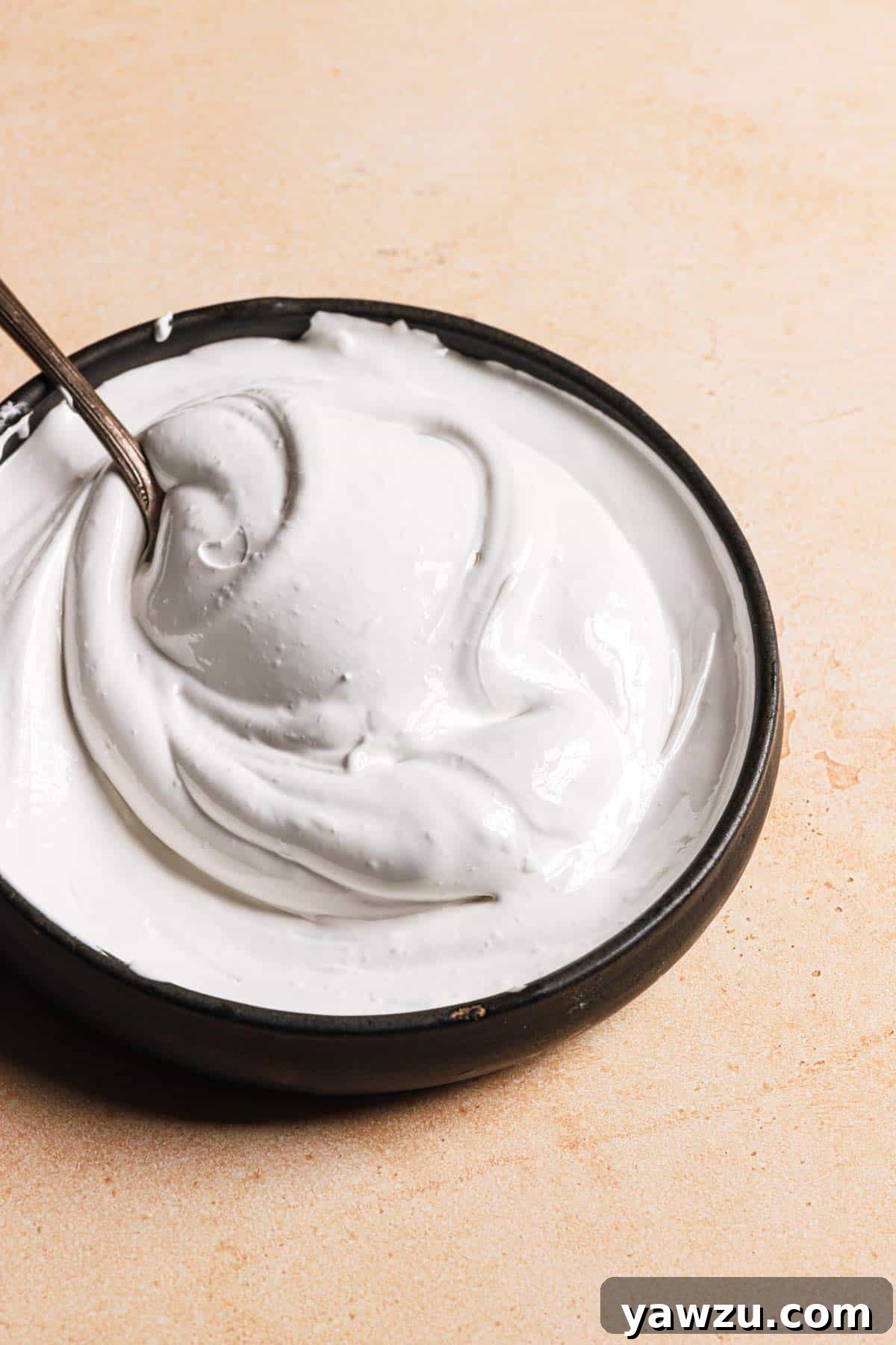 A black bowl filled with marshmallow creme and a silver spoon in the bowl on the left side.