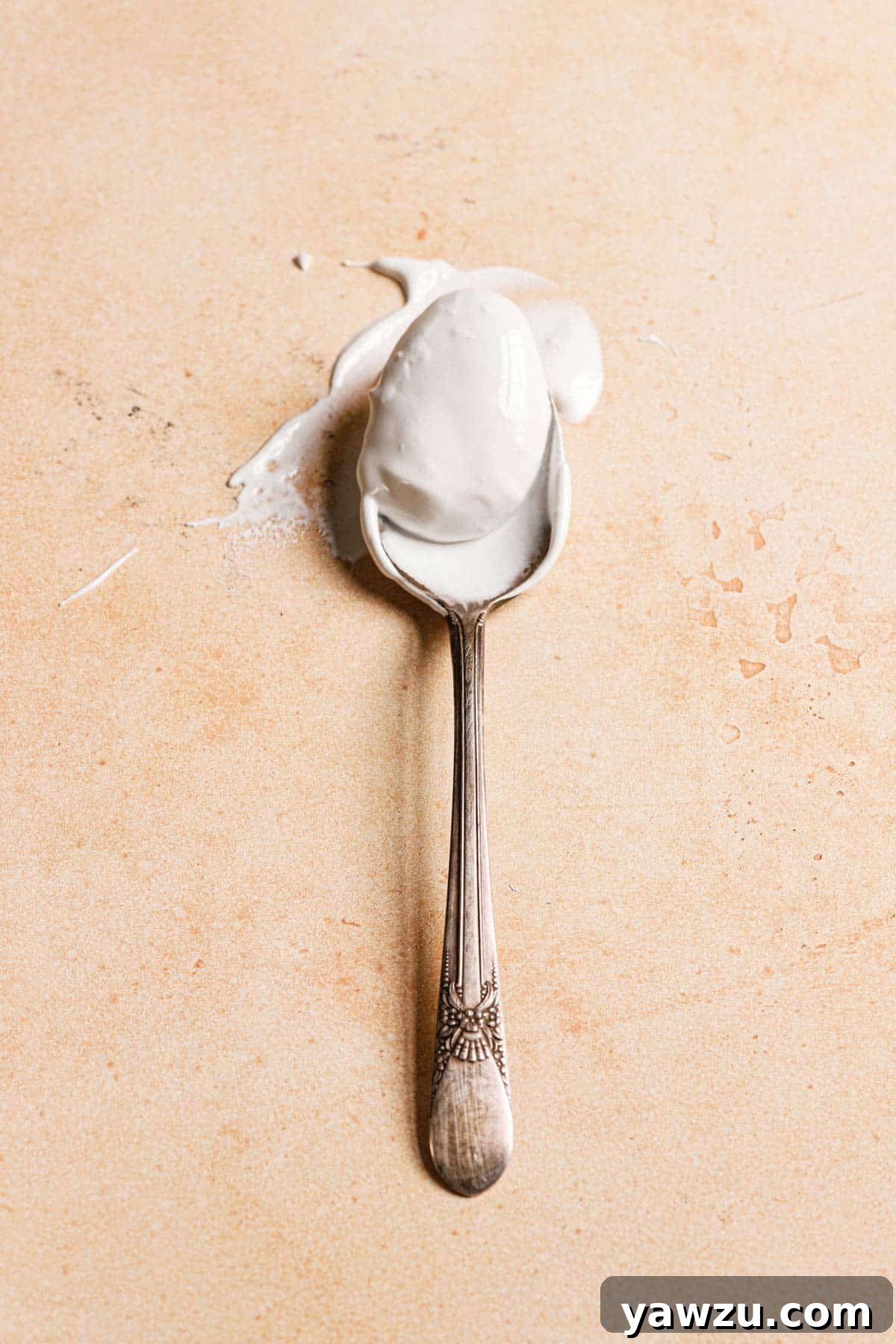 A silver spoon that has been dipped into marshmallow cream on a peach counter.