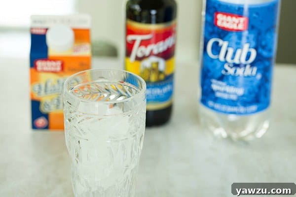 A tall glass filled with ice and effervescent club soda, forming a clear, bubbly base for the Italian cream soda.