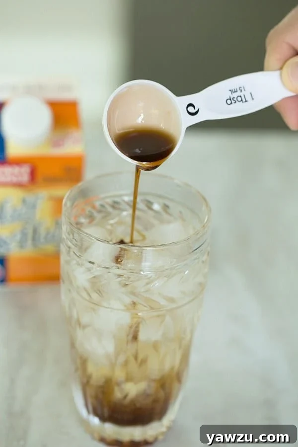 Rich chocolate syrup being artfully drizzled into a glass of bubbly club soda and ice, creating beautiful dark swirls.