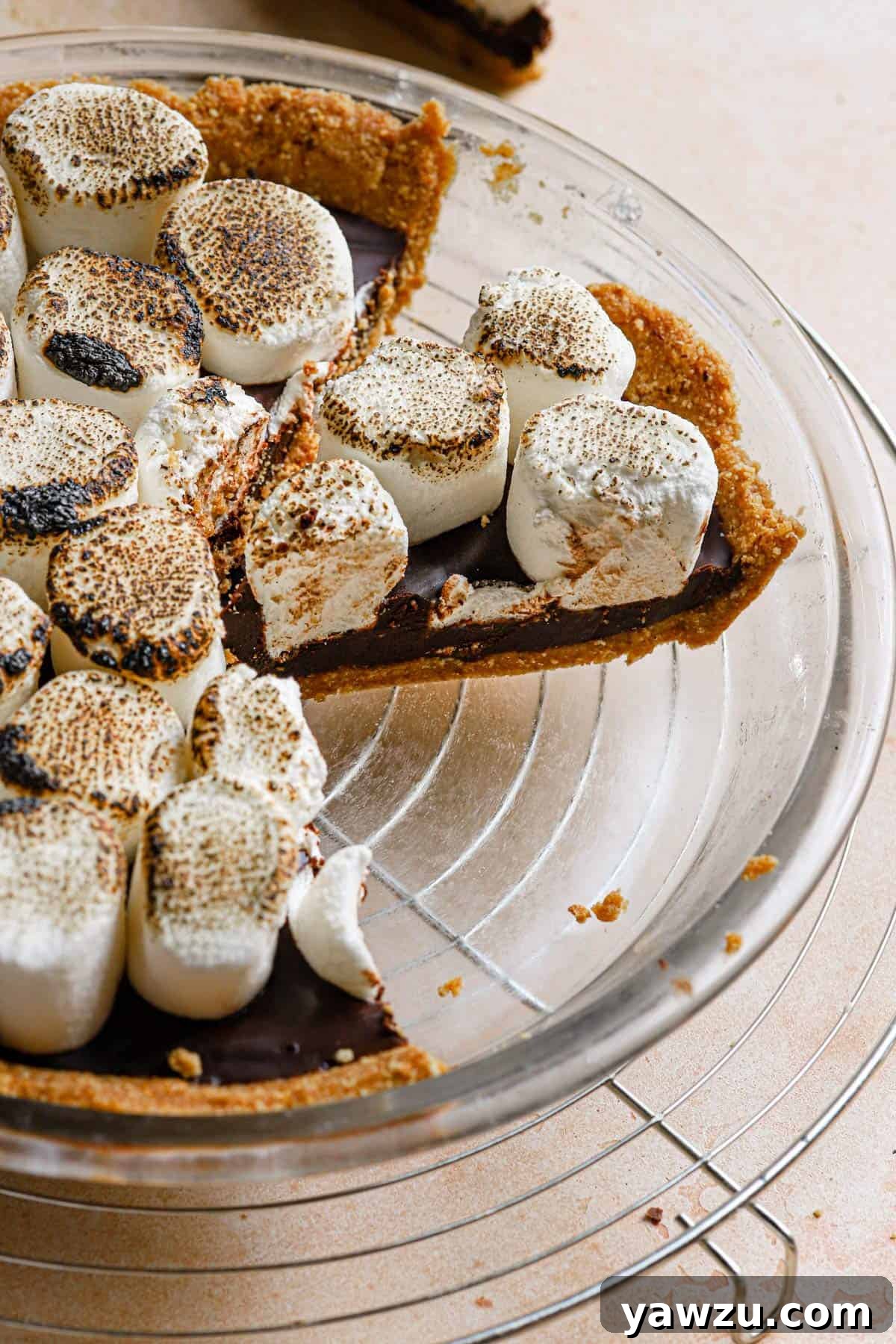 A glass pie plate with a s'mores pie slice from the side to show the layers of the pie.