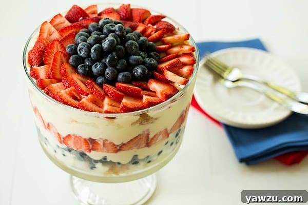 Layers of creamy pudding mixture, fresh blueberries, and sliced strawberries visible in a glass trifle dish, showcasing the Red, White & Blue Berry Trifle