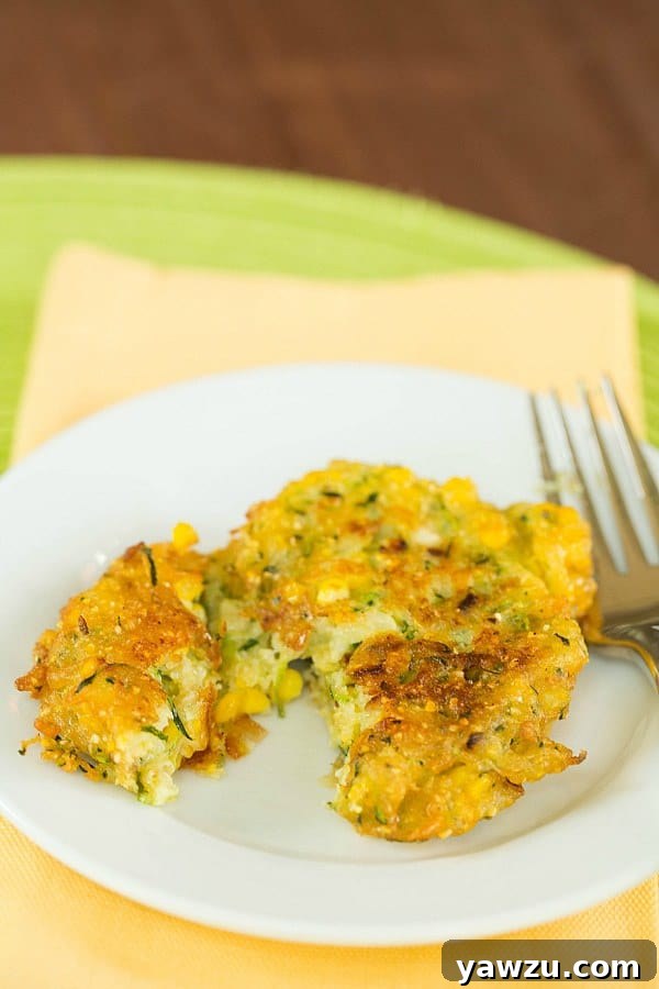 Golden brown Zucchini-Corn Fritters on a plate, garnished with fresh herbs.