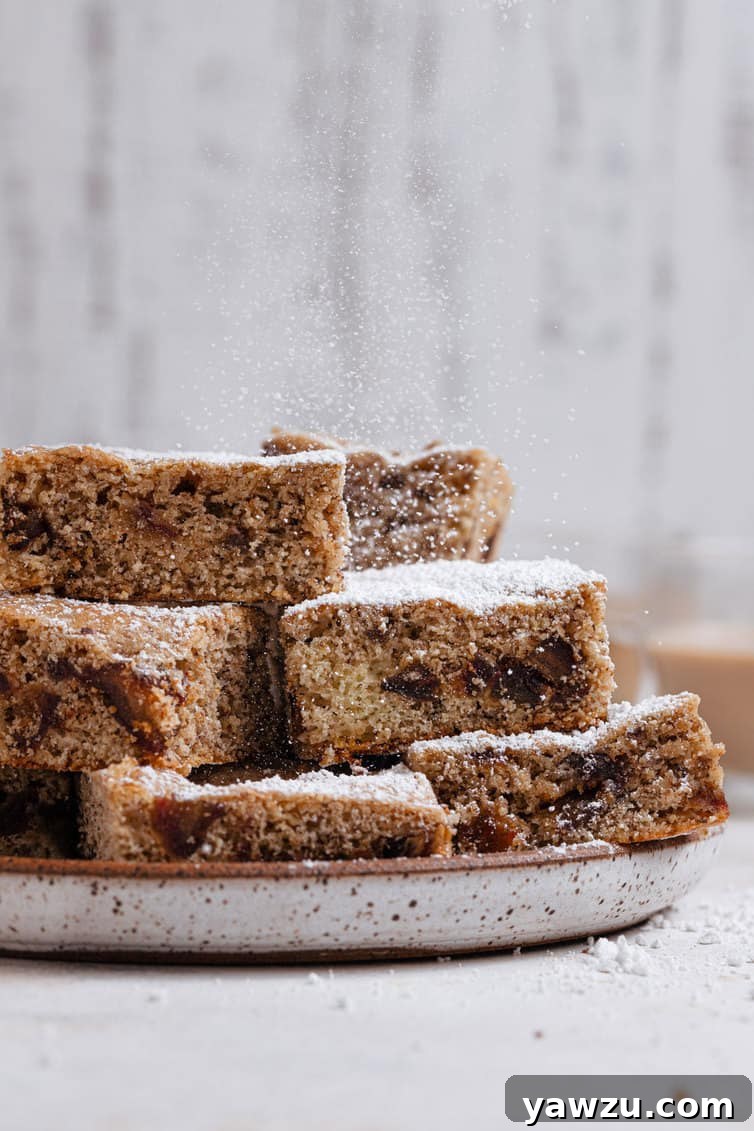 Date bars stacked on a plate and sprinkled with powdered sugar. These classic dessert bars are perfect for any occasion, offering a chewy texture and rich date flavor.