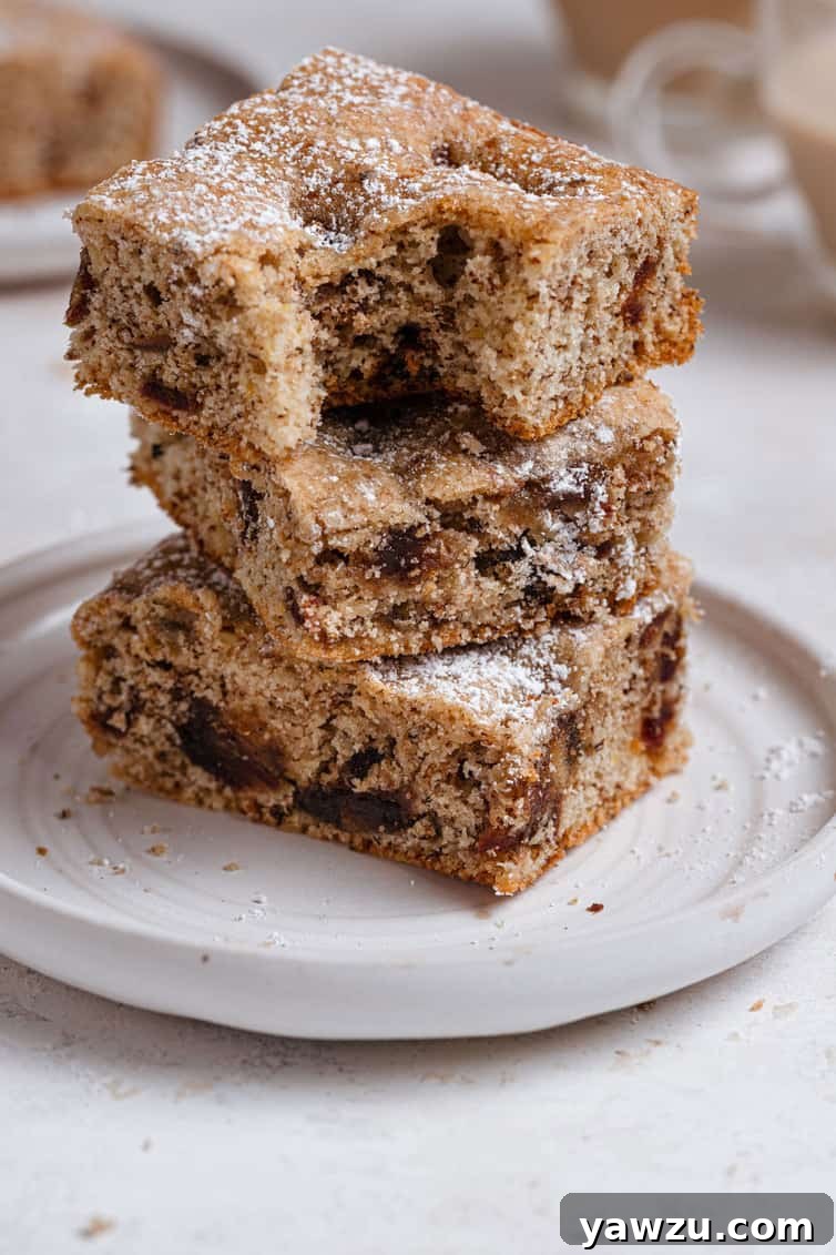 Stack of three date bars with a bite taken out of the top one, revealing the rich date and walnut filling.