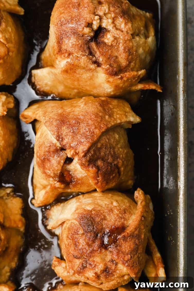 A row of baked apple dumplings glistening with sauce, arranged in a baking dish.