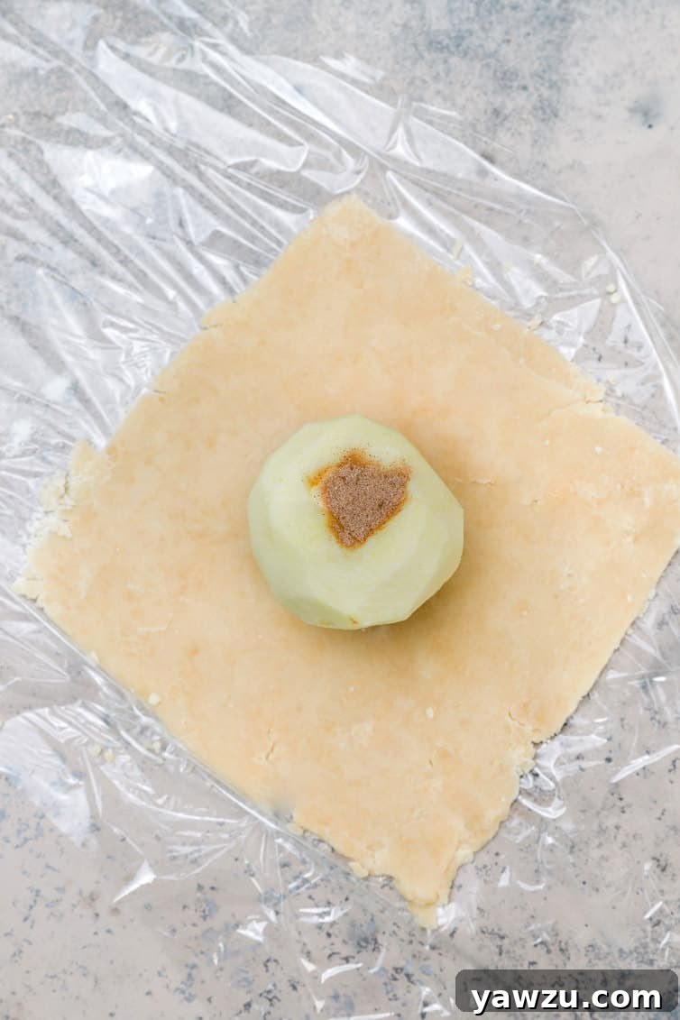 A cored apple, filled with cinnamon-sugar and butter, placed on a square of pastry dough.