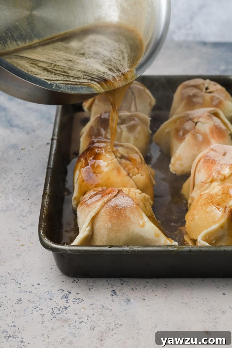 Rich butter-brown sugar sauce being poured over unbaked apple dumplings in a baking pan.