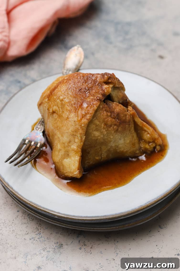 A single baked apple dumpling on a white plate with a fork poised to take a bite.