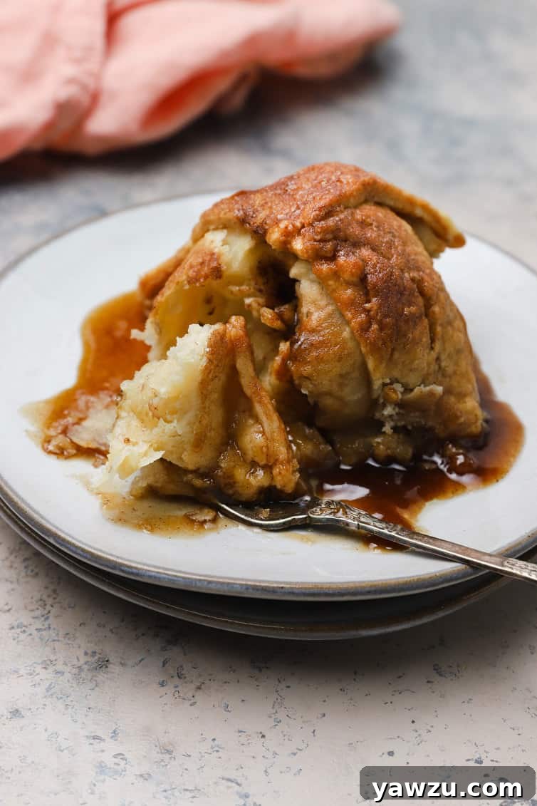 A fork taking a large bite out of a warm, baked apple dumpling, showing the tender apple and flaky pastry.