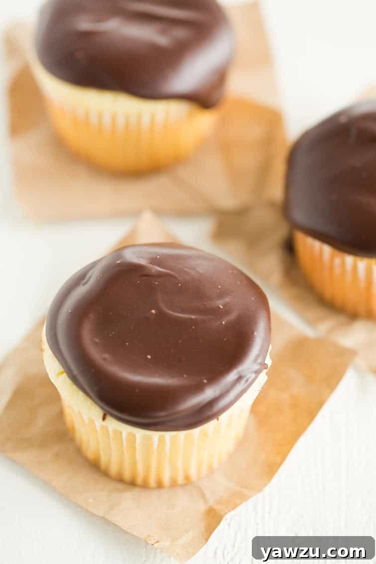 A close-up view of a Boston Cream Cupcake, revealing the perfectly piped pastry cream filling inside the vanilla cake.
