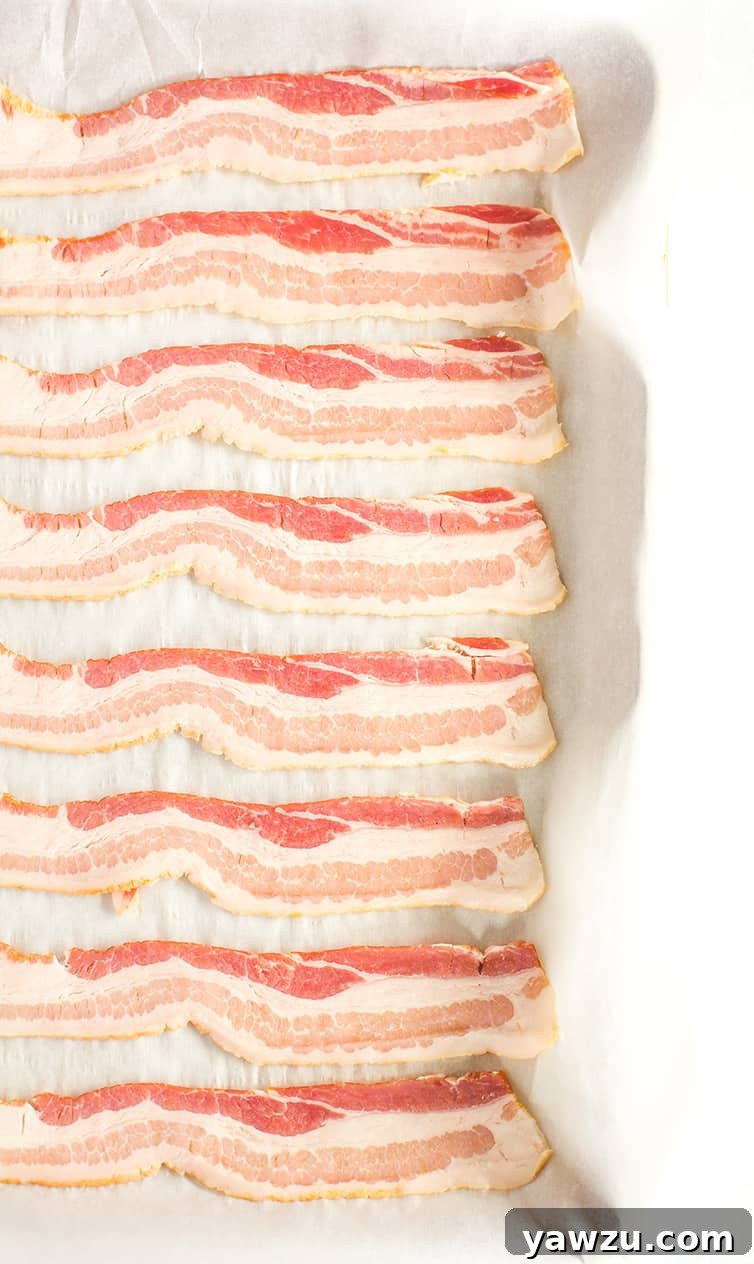 Slices of uncooked bacon meticulously arranged on a parchment-lined baking sheet, ready for the oven.