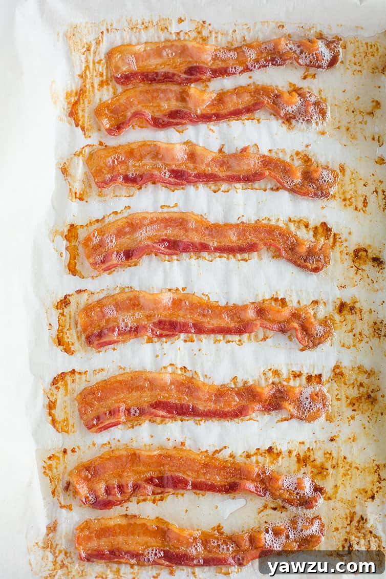 Freshly cooked, perfectly oven baked bacon cooling on a parchment-lined baking sheet, glistening with rendered fat.