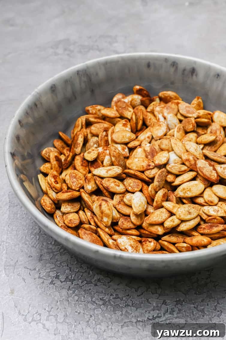 A bowl of roasted pumpkin seeds, garnished with a few whole spices, sits on a rustic wooden surface, evoking the warmth of autumn.