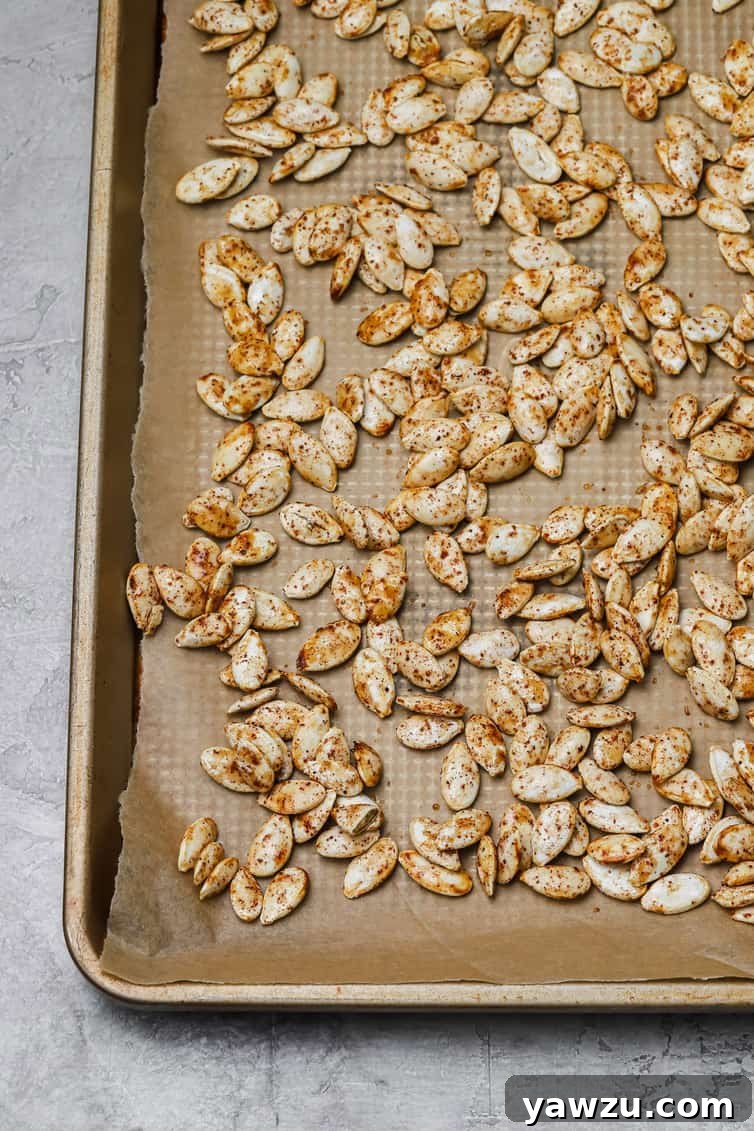 Close-up of seasoned pumpkin seeds evenly spread out on a baking sheet lined with parchment paper, ready for roasting.