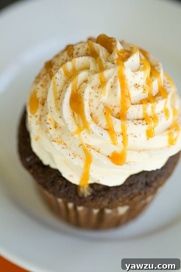 A close-up shot of a single Pumpkin Spice Latte Cupcake garnished with cinnamon and caramel.