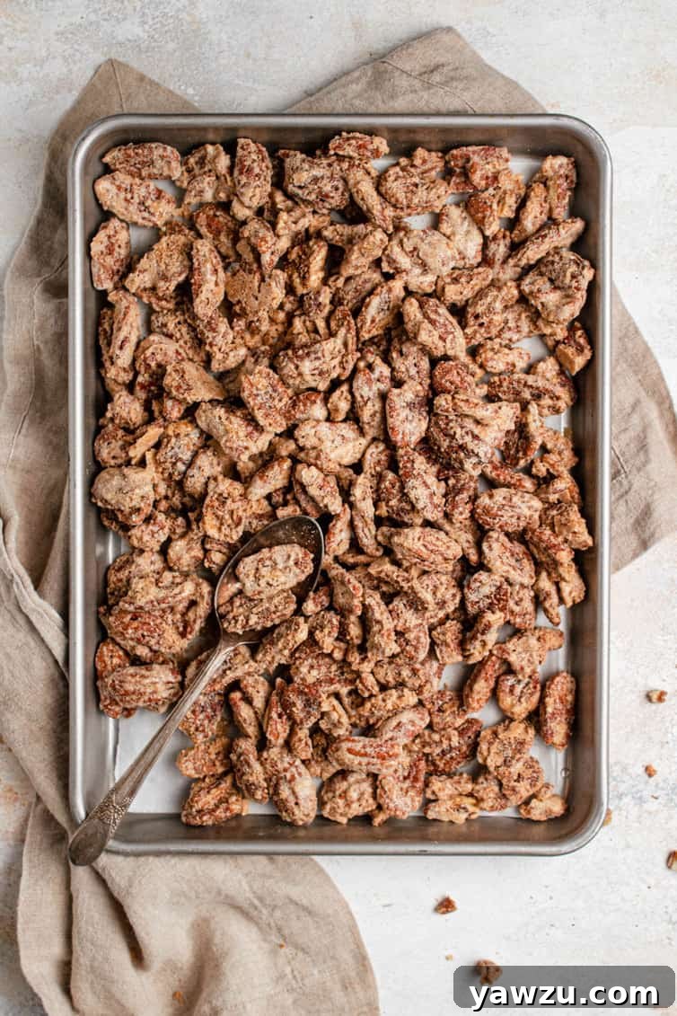A metal baking sheet with candied pecans on a light brown towel on a white counter.