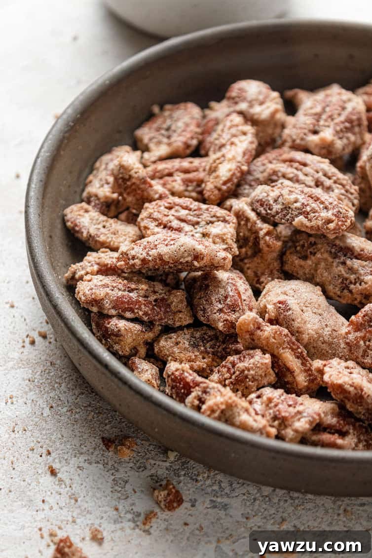 The left half of a brown bowl with cinnamon sugar candied pecans on a white counter.