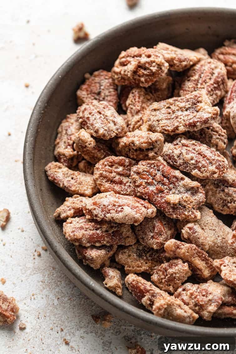A top down photo of the left side of a brown bowl with candied pecans on a white counter.