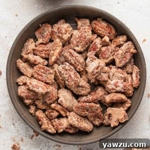 A square photo with candied pecans in a brown bowl on a white counter.