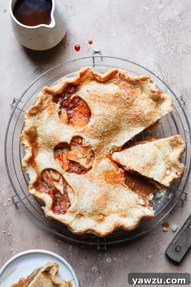 A beautifully baked salted caramel apple pie served in a glass pie dish, with rich caramel sauce visible.
