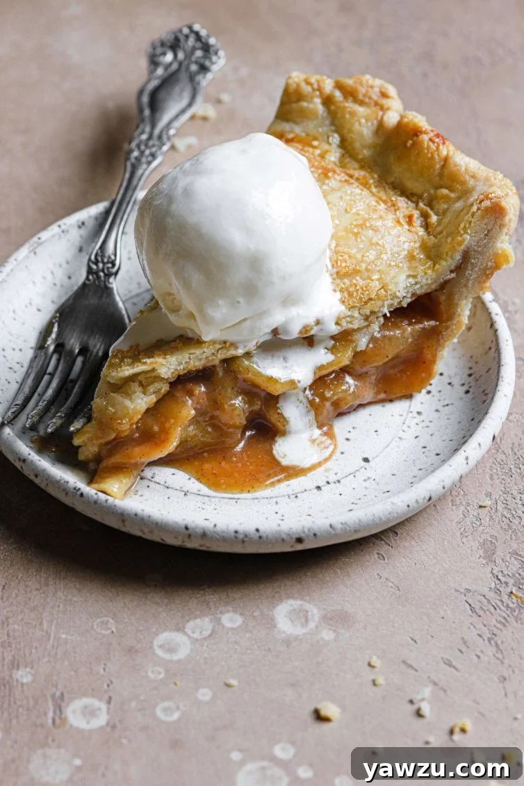 A perfect slice of salted caramel apple pie on a stoneware plate, accompanied by a scoop of vanilla ice cream.