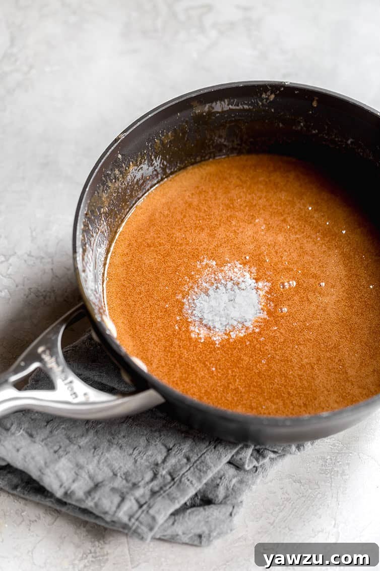 A saucepan filled with freshly made, rich homemade salted caramel sauce, topped with a sprinkle of flaky sea salt.