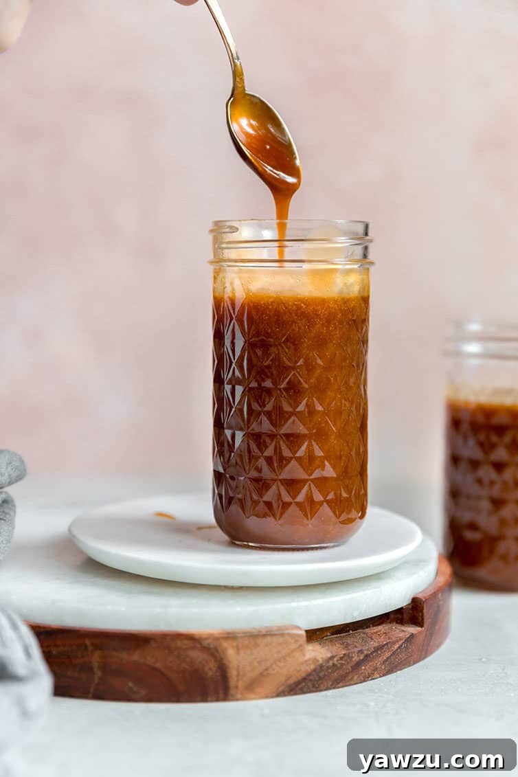 A glass jar filled with luscious homemade salted caramel sauce, with a spoon scooping out a generous portion.