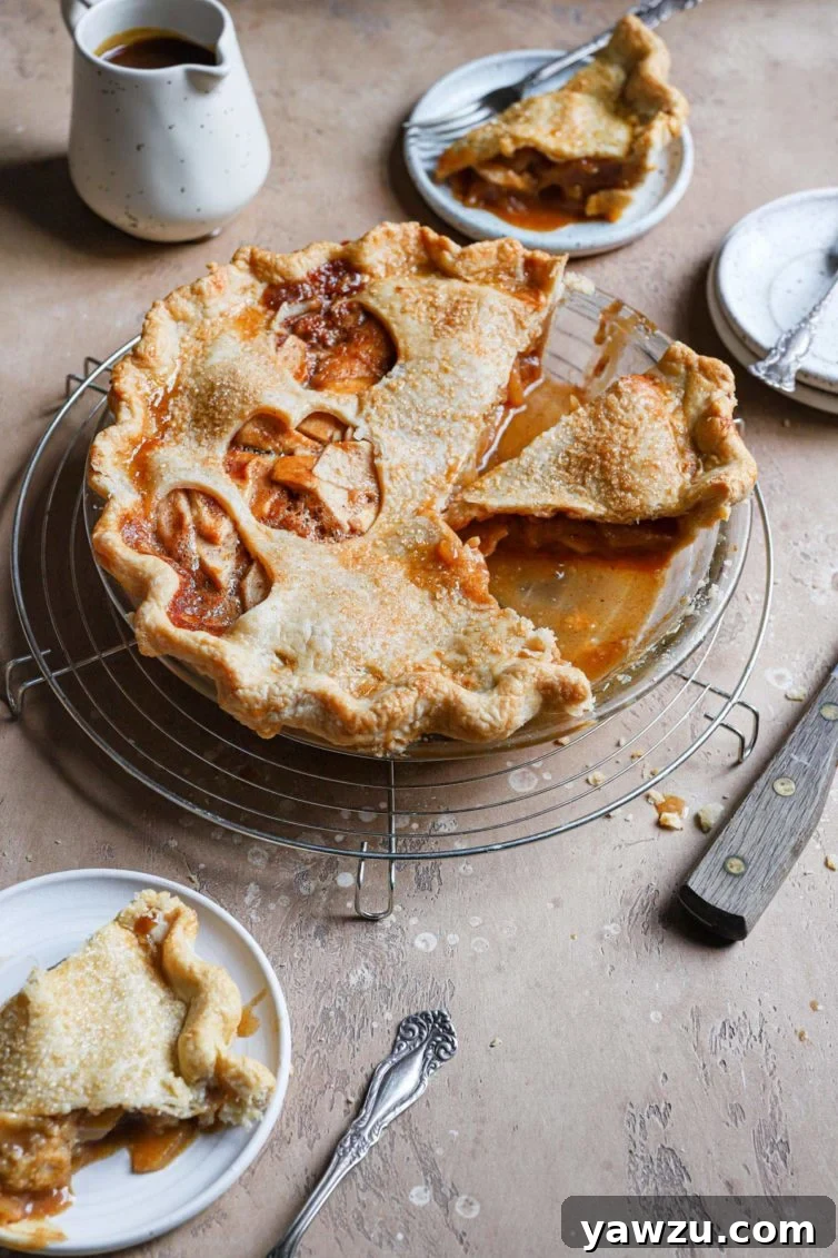 A whole salted caramel apple pie cooling in a glass pie dish, awaiting serving, with caramel bubbling from the top.