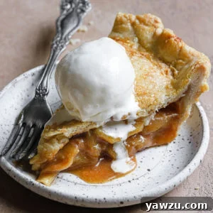 A slice of this salted caramel apple pie served on a stoneware plate with vanilla ice cream