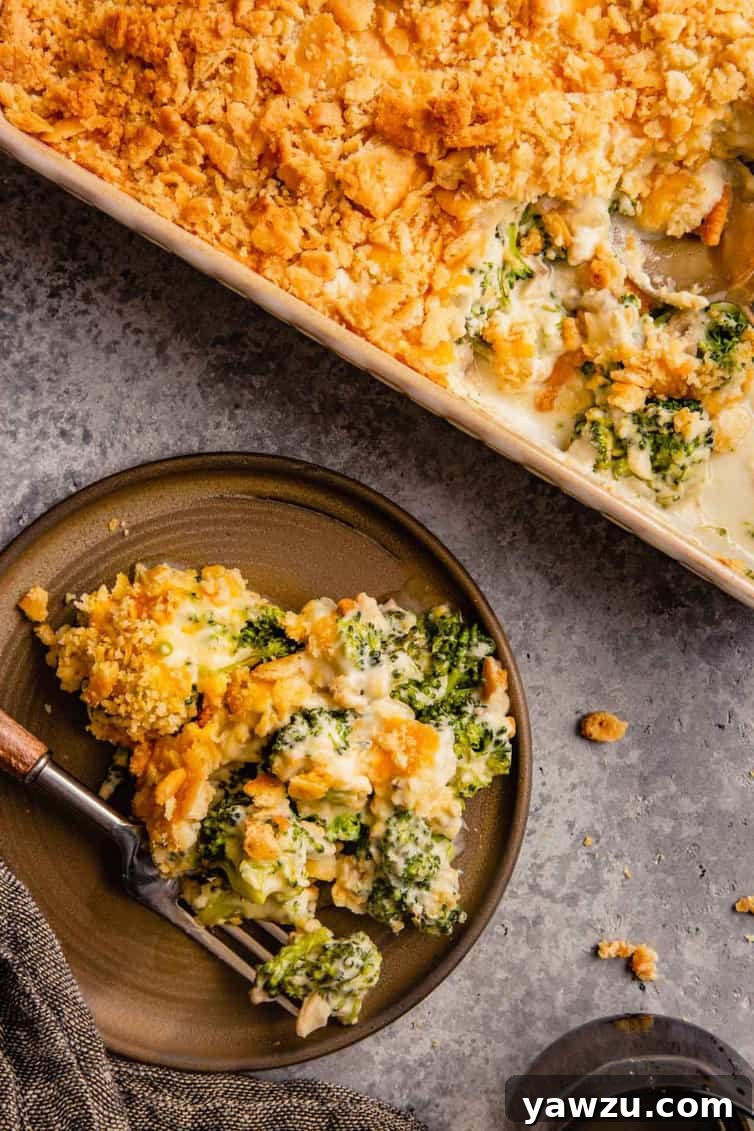A top down picture of broccoli casserole on a brown plate with a fork to the left and a casserole dish to the right, highlighting its golden-brown topping and creamy texture.
