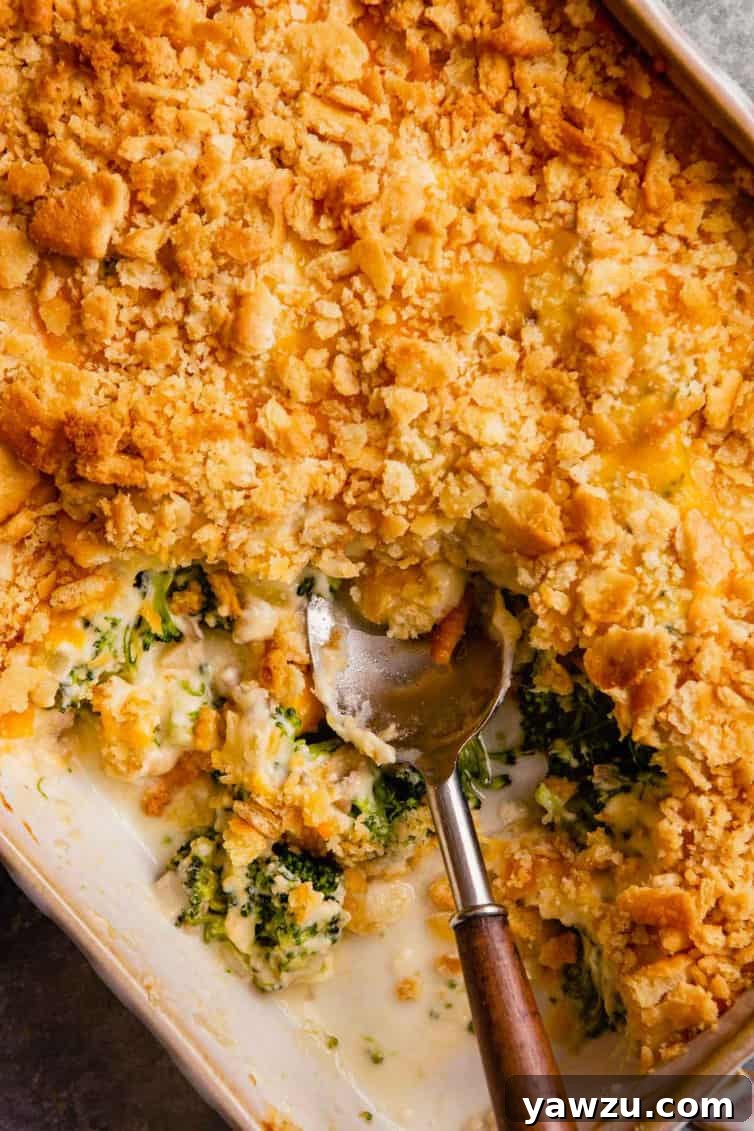 A casserole dish with broccoli casserole, featuring a spoon with a wooden handle having taken a scoop out, showcasing the creamy interior and crunchy topping.