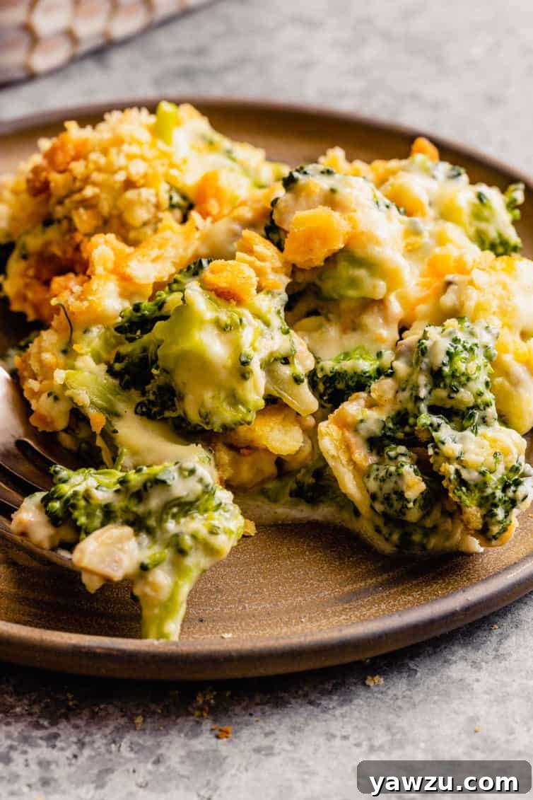 A picture from the side of broccoli casserole served on a brown plate, resting on a gray counter, showing the layers of topping and creamy interior.