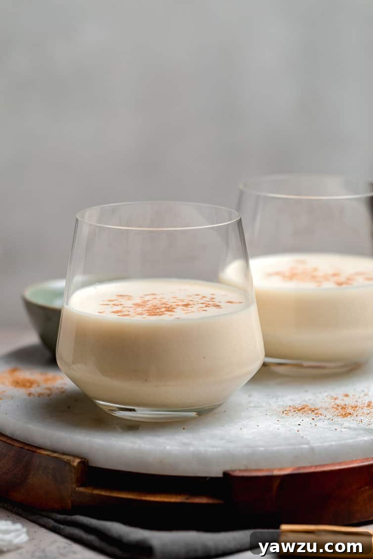 Two glasses half-filled with eggnog and a sprinkle of nutmeg.