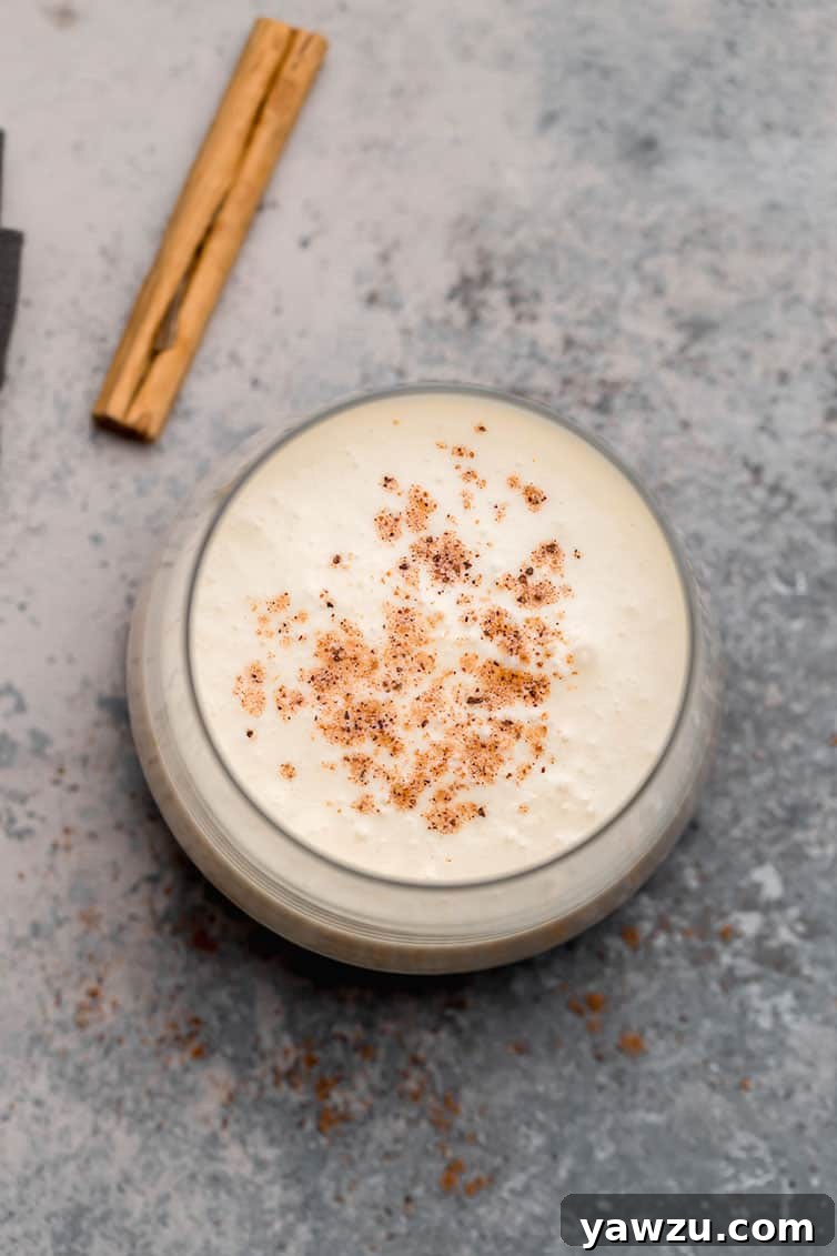 An overhead shot of a glass of eggnog with a sprinkle of nutmeg on top.